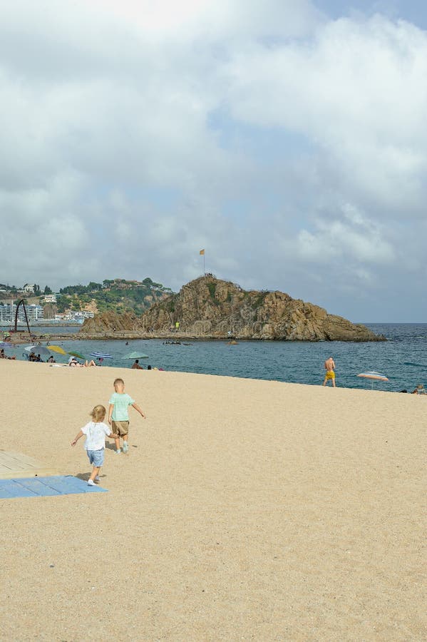 Blanes, Catalonia, Spain September 4 2022: Boy and girl going down to the beach to play. Sunny day with an island in the background and the sea. Umbrellas on the beach and few people relaxing. Blanes, Catalonia, Spain September 4 2022: Boy and girl going down to the beach to play. Sunny day with an island in the background and the sea. Umbrellas on the beach and few people relaxing