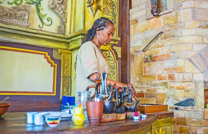 KIEV, UKRAINE - JUNE 4, 2017: The young Ethiopian girl roasts coffee beans for the coffee ceremony at the bar counter of traditional cafe, on June 4 in Kiev. KIEV, UKRAINE - JUNE 4, 2017: The young Ethiopian girl roasts coffee beans for the coffee ceremony at the bar counter of traditional cafe, on June 4 in Kiev.