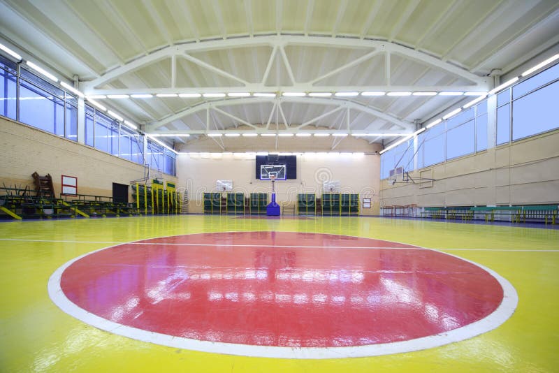 On red circle of red-yellow floor inside lighted school gym hall with basket. On red circle of red-yellow floor inside lighted school gym hall with basket