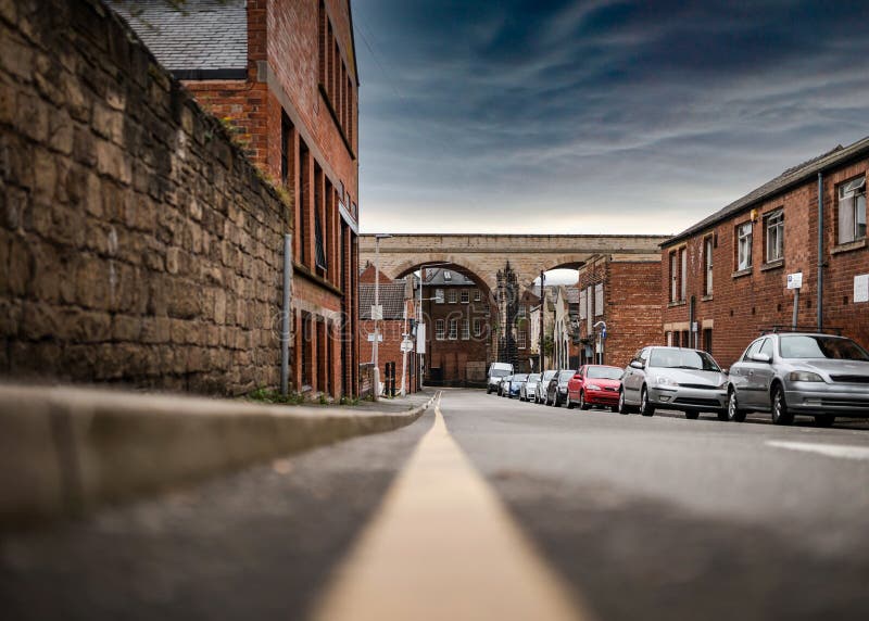 No parking restrictions yellow line on road low angle showing cars parked on busy town street scene. Railway arches bridge shops.