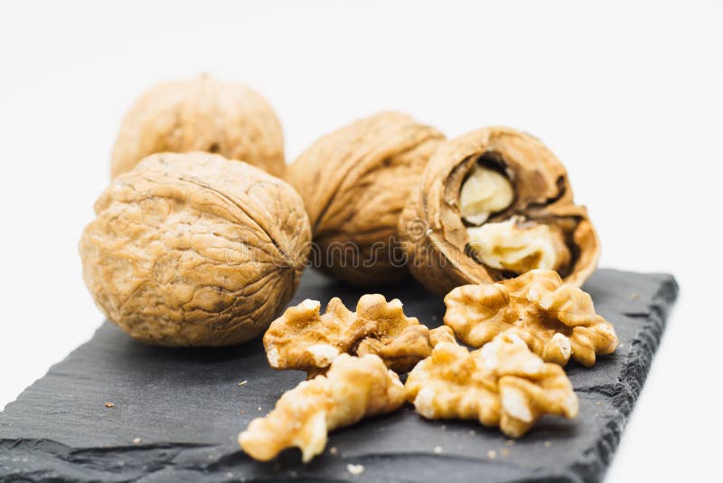 Several walnuts both in their shells and &#x28;un&#x29; shelled on black slate stone plate, whole setup isolated on white. Several walnuts both in their shells and &#x28;un&#x29; shelled on black slate stone plate, whole setup isolated on white