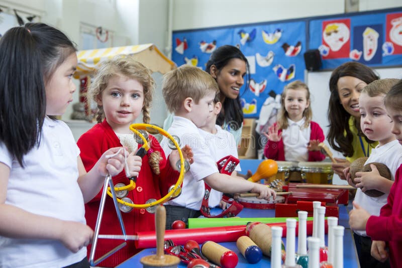 Nursery children playing with musical instruments in the classroom. One little girl is looking at the camera with a tambourine. Nursery children playing with musical instruments in the classroom. One little girl is looking at the camera with a tambourine.