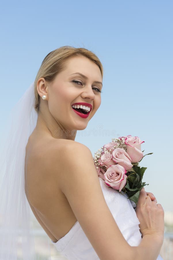 Side view portrait of cheerful young bride with flower bouquet against clear blue sky. Side view portrait of cheerful young bride with flower bouquet against clear blue sky