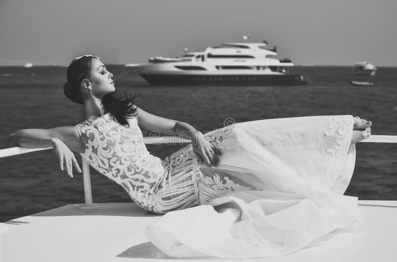 Noiva da mulher no vestido de casamento que relaxa no iate no mar imagem de stock Noiva da mulher no vestido de casamento que relaxa no iate no mar imagem de stock