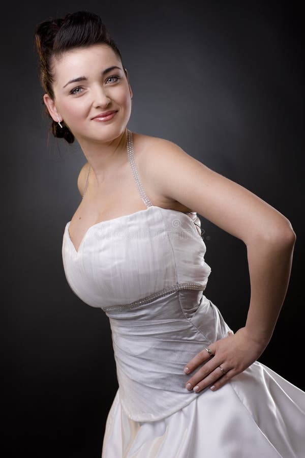 Happy bride standing with arm on hips in a white wedding dress, smiling and looking at camera. Happy bride standing with arm on hips in a white wedding dress, smiling and looking at camera.