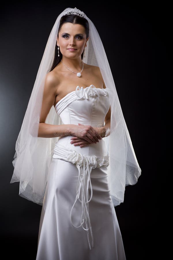 Studio portrait of a young bride wearing white wedding dress with veil, smiling and looking at camera. Studio portrait of a young bride wearing white wedding dress with veil, smiling and looking at camera.