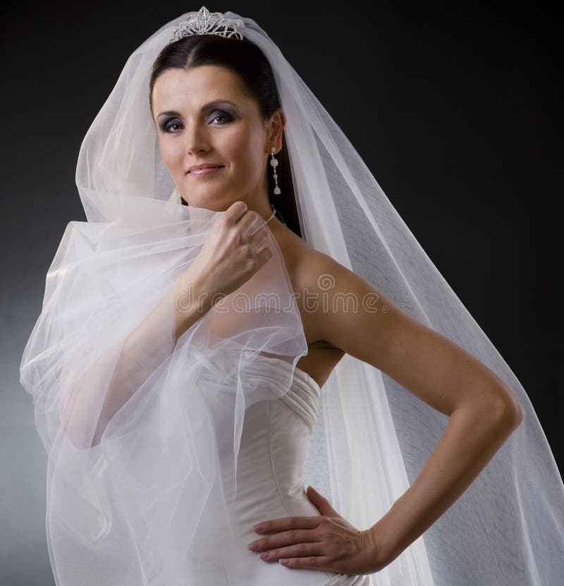 Portrait of a smiling young bride wearing a white wedding dress, holding her veil lloking at camera. Portrait of a smiling young bride wearing a white wedding dress, holding her veil lloking at camera.