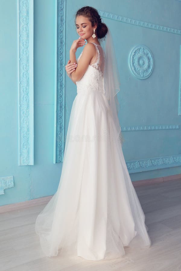 Noiva nova bonita com cabelo encaracolado escuro no vestido de casamento luxuoso que levanta na sala fotos de stock Noiva nova bonita com cabelo encaracolado escuro no vestido de casamento luxuoso que levanta na sala fotos de stock