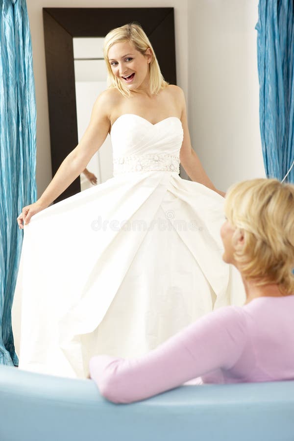 Bride trying on wedding dress with sales assistant looking excited. Bride trying on wedding dress with sales assistant looking excited