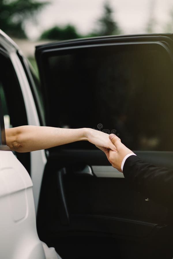 Noivo feliz que ajuda sua noiva bonita fora do carro do casamento fotografia de stock Noivo feliz que ajuda sua noiva bonita fora do carro do casamento fotografia de stock