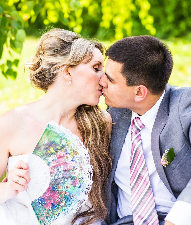 Noivos bonitos que sentam-se na grama e no beijo Pares novos do casamento fotos de stock Noivos bonitos que sentam-se na grama e no beijo Pares novos do casamento fotos de stock
