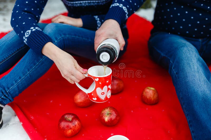Το άτομο χύνει το τσάι σε μια κούπα με μια εικόνα της καρδιάς Τα νέα ζεύγη στα πουλόβερ κάθονται στο κόκκινο κάλυμμα Γαμήλιο πικ- στοκ φωτογραφίες με δικαίωμα ελεύθερης χρήσης