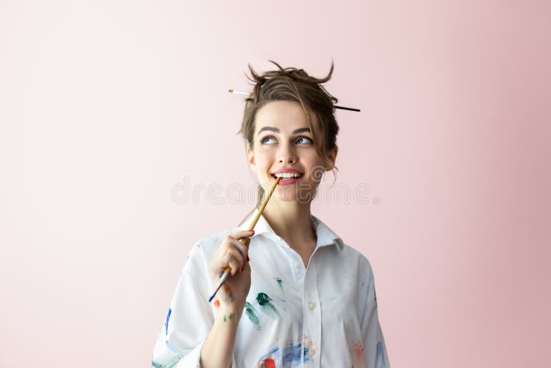 美丽的年轻女子在幸福的梦中咬着画笔 库存照片