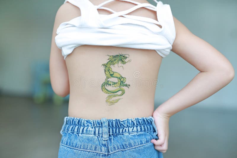 小女孩背部的肖像，皮肤上贴着龙纹身贴纸。装扮纹身 图库摄影