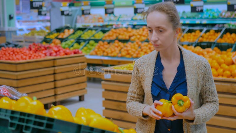 Женщина покупает свежие апельсиновые перцы в продуктовом магазине стоковое фото rf