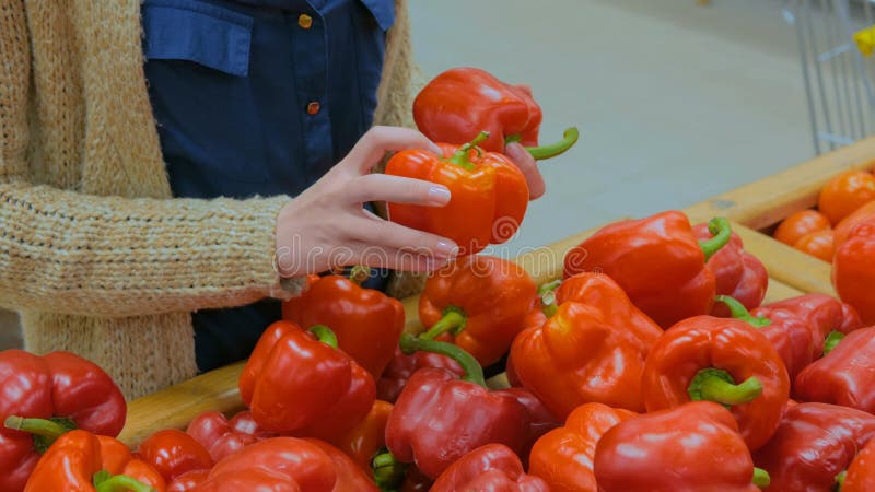Женщина покупает свежие красные перцы в продуктовом магазине стоковые фото