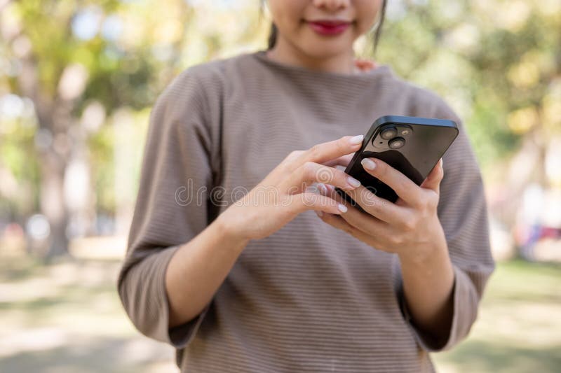 在公园里散步时，一个女人在智能手机上与朋友聊天，一片片子被拍到 图库摄影