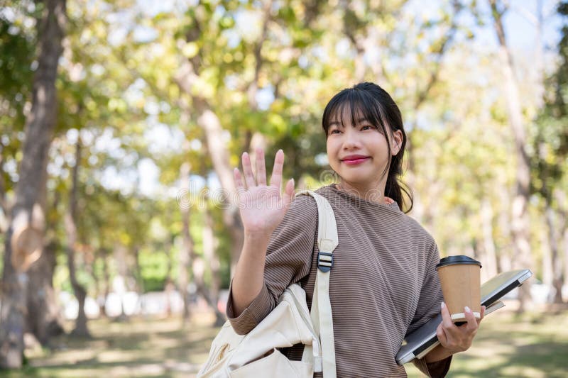 一位友善的女学生正在公园里向她的朋友挥手，表示问候或告别 库存图片