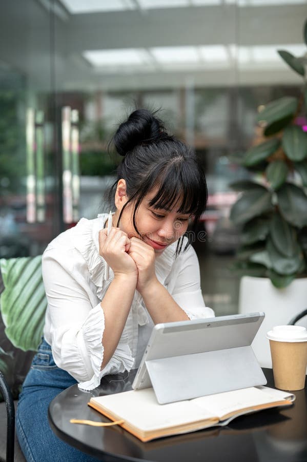 年轻快乐的亚洲女性正享受着在咖啡馆里阅读其数字平板电脑上的东西 库存照片
