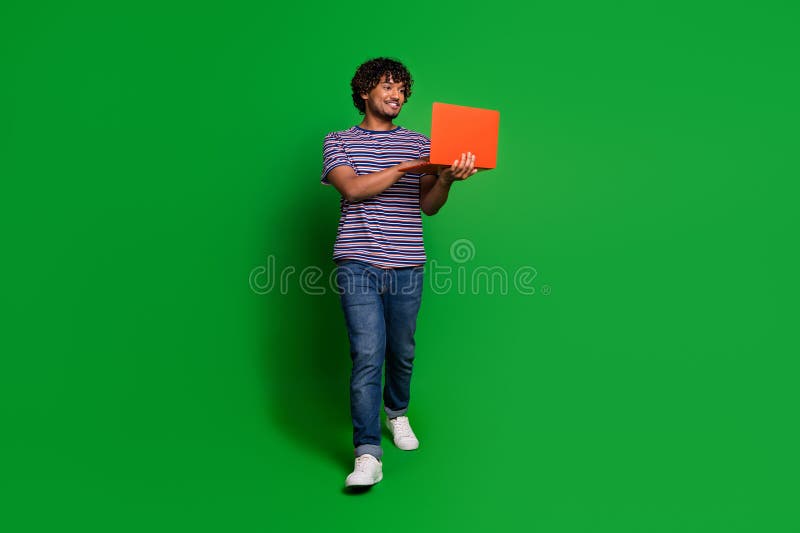 Фотопортрет молодого опытного индийского программиста, работающего онлайн с ноутбуком и идущего в одиночестве на зеленом фоне стоковая фотография