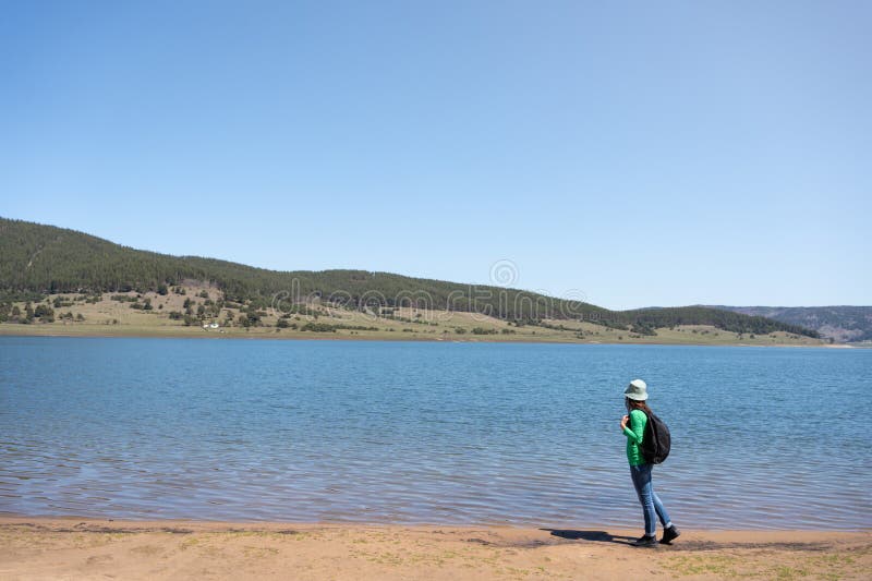 年轻女子背着背包沿着山湖行走。生态旅游,徒步旅行。巴塔克湖,罗多皮山脉,保加利亚 免版税库存图片