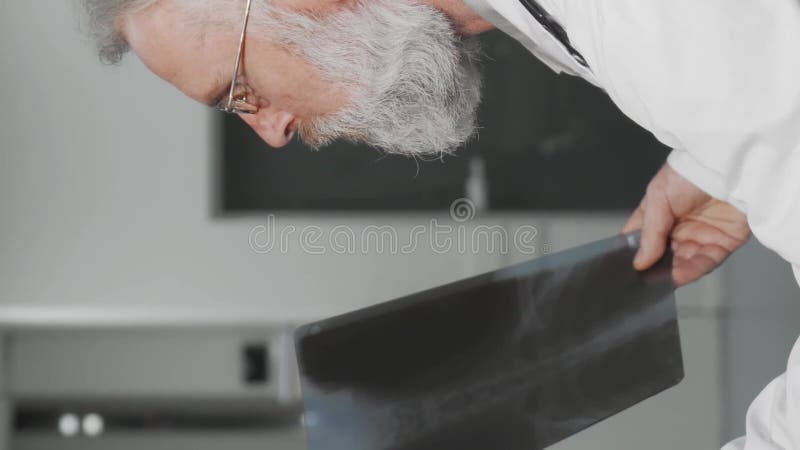 Ανώτερος γιατρός χαμογελά στην κάμερα ενώ εξετάζει ακτινογραφίες απόθεμα βίντεο