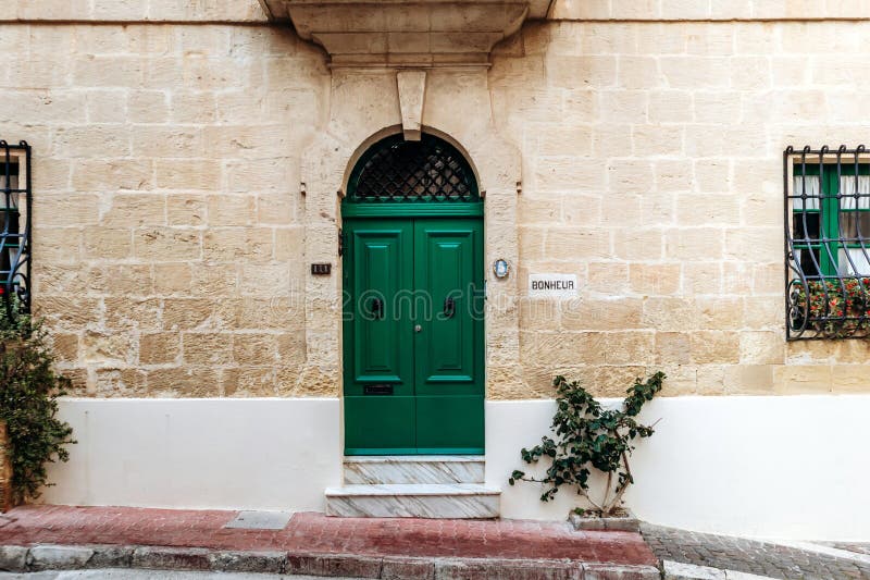 Μια ζωντανή πράσινη διπλή πόρτα με χερούλια κεφαλών λιονταριών, ενσωματωμένη σε έναν κίτρινο ασβεστολιθικό τοίχο στοκ εικόνα με δικαίωμα ελεύθερης χρήσης