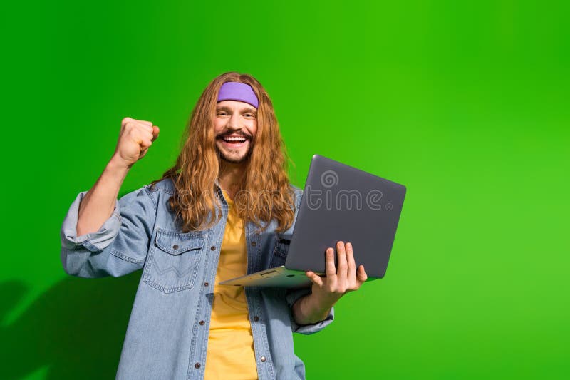 Νέος άνδρας με φορητό υπολογιστή που κάνει μια χειρονομία με γροθιά σε πράσινο φόντο, αποπνέοντας χαρά και επιτυχία στοκ εικόνες