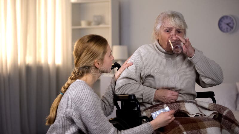 Nonna che prende pillola con acqua, nipote preoccupantesi che sostiene donna malata fotografia stock libera da diritti Nonna che prende pillola con acqua, nipote preoccupantesi che sostiene donna malata fotografia stock libera da diritti