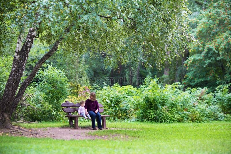 Nonna e neonata in parco sul banco sotto il grande albero immagine stock libera da diritti Nonna e neonata in parco sul banco sotto il grande albero immagine stock libera da diritti