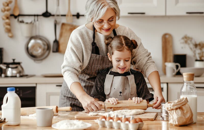Nonna e nipotina di famiglia felici cucinano in cucina i biscotti al forno in impasto. Nonna e nipote cucine cuociono in cucina impasto in ginocchio e biscotti al forno