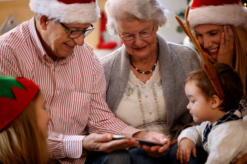 Nonni con i bambini che guardano le foto di Natale sul fon delle cellule immagine stock libera da diritti Nonni con i bambini che guardano le foto di Natale sul fon delle cellule immagine stock libera da diritti