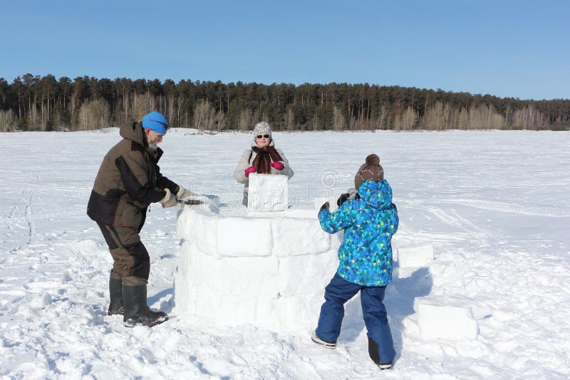 Nonno, nonna felice e nipote costruenti un iglù su una radura nevosa nell'inverno immagine stock libera da diritti Nonno, nonna felice e nipote costruenti un iglù su una radura nevosa nell'inverno immagine stock libera da diritti