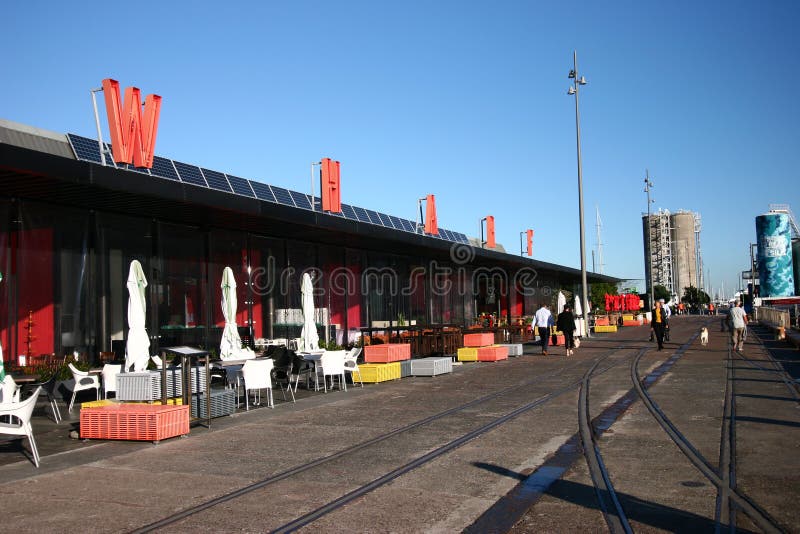 Modification of repository restored into sightseeing destination in North Wharf, Wynyard Quarter, Auckland, New Zealand. Redevelopment of cargo storehouse converted into restaurants with outdoor seating, and abandoned train rails on pedestrian boardwalk. Transformation of old building redeveloped into eateries with exterior seats, and decommissioned rail tracks on promenade. Remodeling of dockside depository transformed into cafes with outside chairs, and railroad tracks on pathway. Conversion of freight depot rebuilt into popular tourist attraction in docklands.  Restoration of storage architecture renovated into bars. Rebuilding of architectural landmark modified into dinning. road street path walk passage passageway. Modification of repository restored into sightseeing destination in North Wharf, Wynyard Quarter, Auckland, New Zealand. Redevelopment of cargo storehouse converted into restaurants with outdoor seating, and abandoned train rails on pedestrian boardwalk. Transformation of old building redeveloped into eateries with exterior seats, and decommissioned rail tracks on promenade. Remodeling of dockside depository transformed into cafes with outside chairs, and railroad tracks on pathway. Conversion of freight depot rebuilt into popular tourist attraction in docklands.  Restoration of storage architecture renovated into bars. Rebuilding of architectural landmark modified into dinning. road street path walk passage passageway