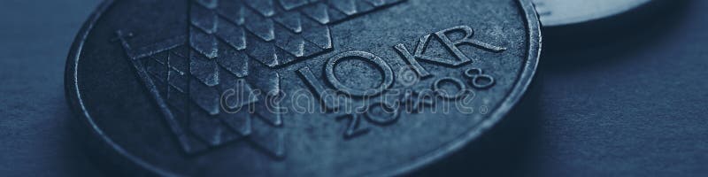 Norwegian coins lie on gray surface. 10 Norges kroner coin close up. National currency of Norway. Banking and credit. Dark blue tinted banner or header for news about economy or finance. Macro