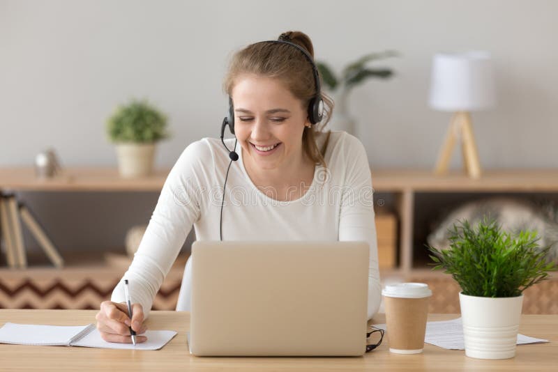 Notas sonrientes de la escritura de las auriculares de la mujer que llevan que estudian en línea en el ordenador portátil