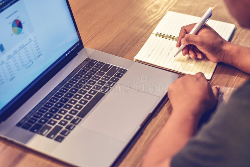 Note adulte d'écriture d'homme sur un carnet près d'ordinateur portable sur un bureau dans le bureau image stock Note adulte d'écriture d'homme sur un carnet près d'ordinateur portable sur un bureau dans le bureau image stock