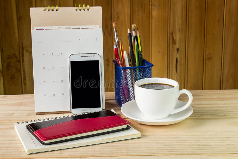 Note book,smart phone,coffee cup,and stack of book with calendar