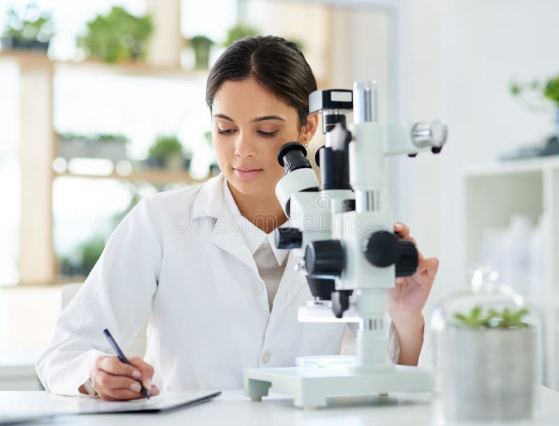 Note d'une nouvelle percée. un jeune scientifique écrit des notes en utilisant un microscope dans un laboratoire.