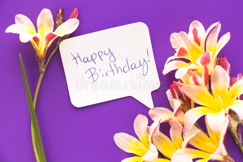 Note in shape of heart with words `Happy Birthday!` with flowers on purple surface. Note in shape of heart with words `Happy Birthday!` with flowers on purple surface.