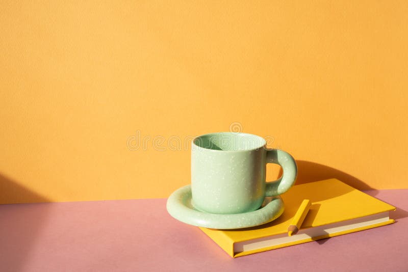 Notebook and colored pencil, coffee cup on pink desk. orange wall background. workspace. studio shot