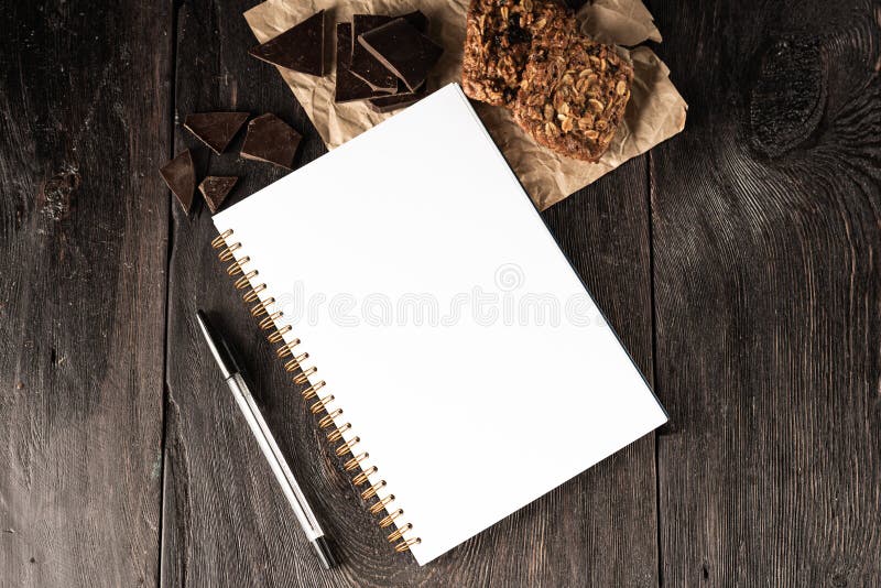 Notebook for culinary notes and a pen on the table. muffins and pieces of chocolate on the table. Cook business concept. Page, laptop.