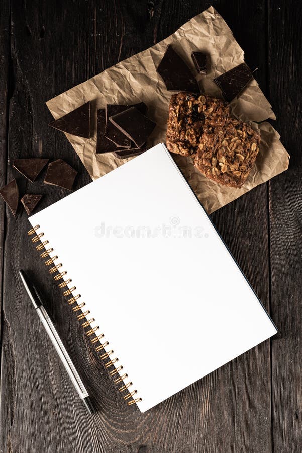 Notebook for culinary notes and a pen on the table. muffins and pieces of chocolate on the table. Cook business concept.