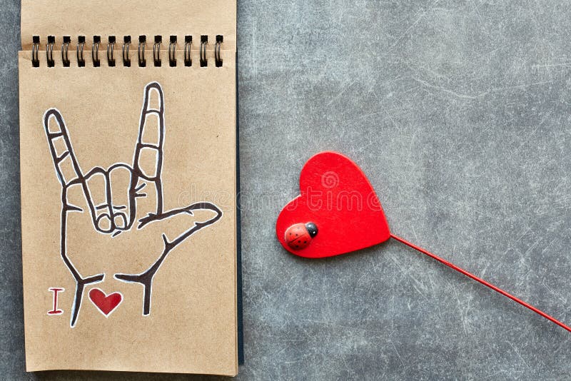 A notebook of Kraft paper, with a painted ASL American sign language symbol I Love you ILY and a wooden red heart with a small stock image A notebook of Kraft paper, with a painted ASL American sign language symbol I Love you ILY and a wooden red heart with a small stock image