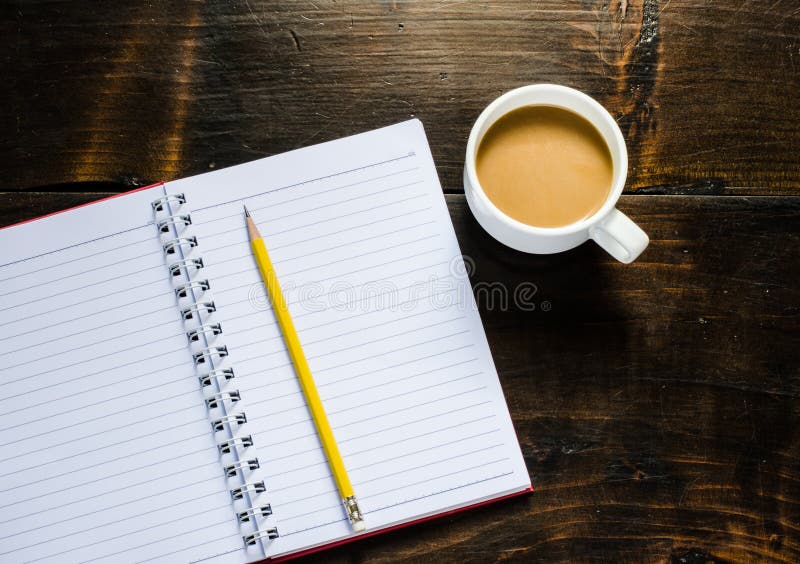 Notebook pen and cup of coffee in wood table