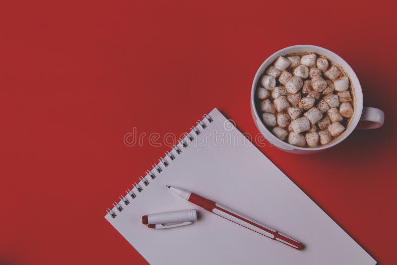 A notebook and pen for planning and making a list lie on a red background, next to it is a mug with hot coffee or chocolate stock photo