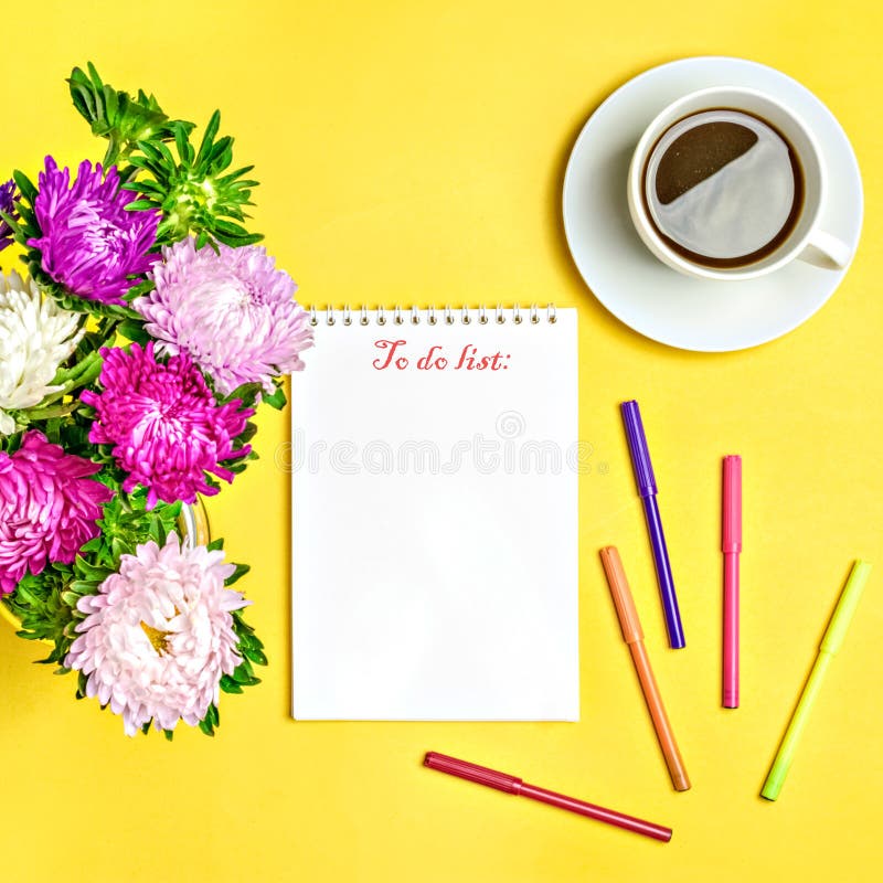 Notepad , aster flowers, colored felt-tip pens, cup with coffee on yellow background. Concept autumn, summer, spring.