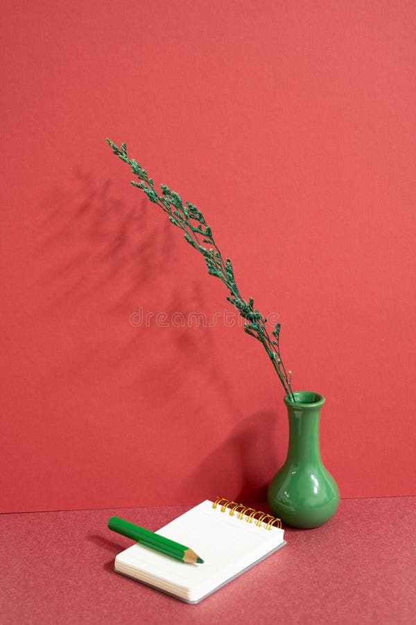 Notepad and colored pencil with vase of plant on red desk. red wall background, workspace. studio shot