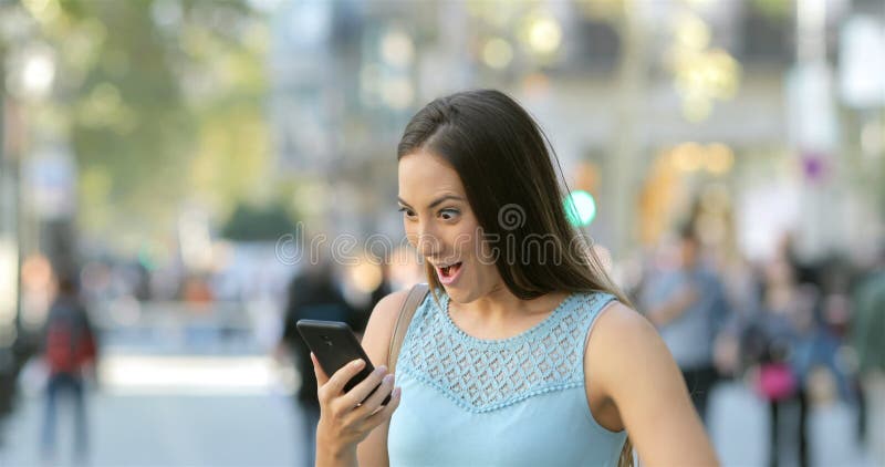 Noticias emocionadas de la lectura de la mujer en un teléfono en la calle