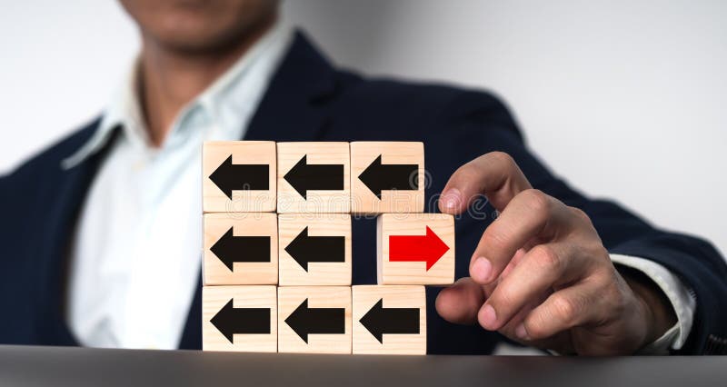 The notion of a businessman\ s hand holding a wooden block with a red arrow pointing in one direction and a black arrow.